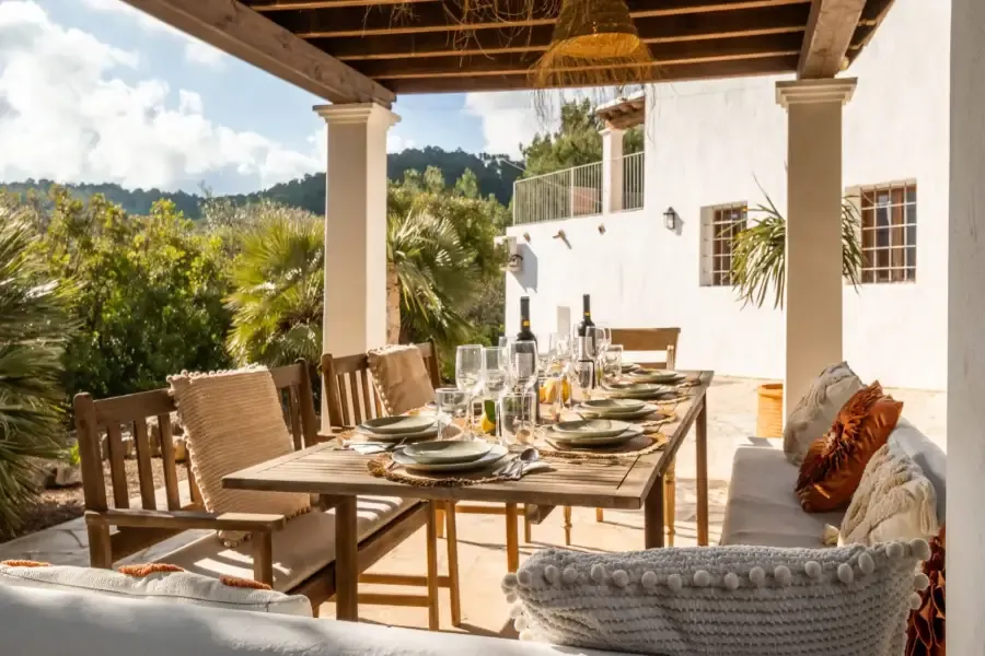Een gedekte buitentafel op een terracota terras onder een rieten dak; in de achtergrond zicht op de bergen van Ibiza